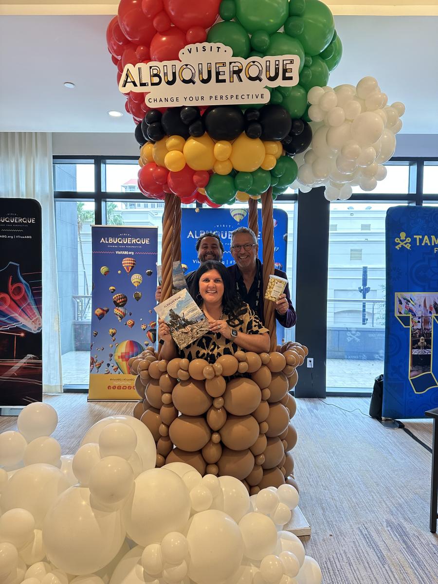 Three people stand in a hot air balloon made from balloons at the 2025 PRSA Travel and Tourism conference.