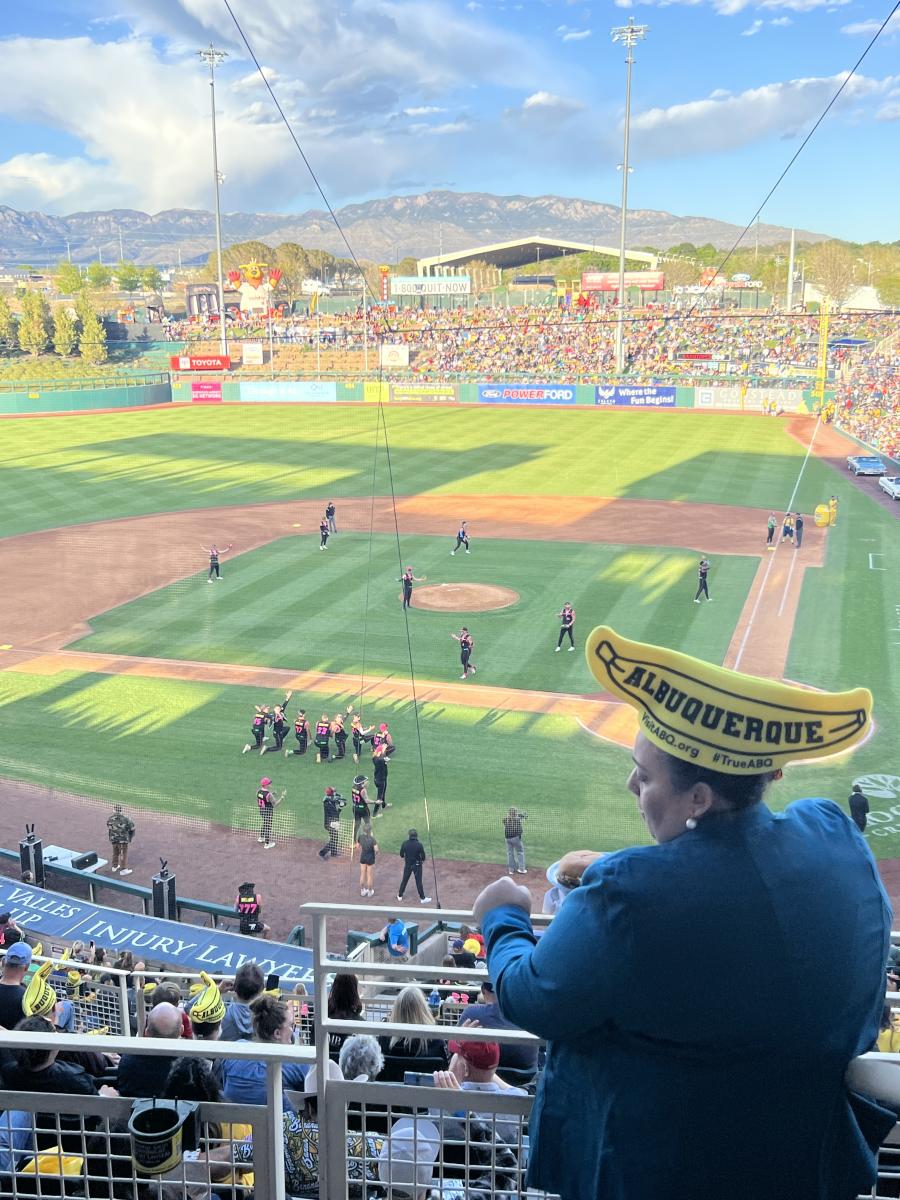 Someone stands up in the stands of Isotopes Park during the Savannah Bananas game. She is wearing a banana hat created by Visit Albuquerque.