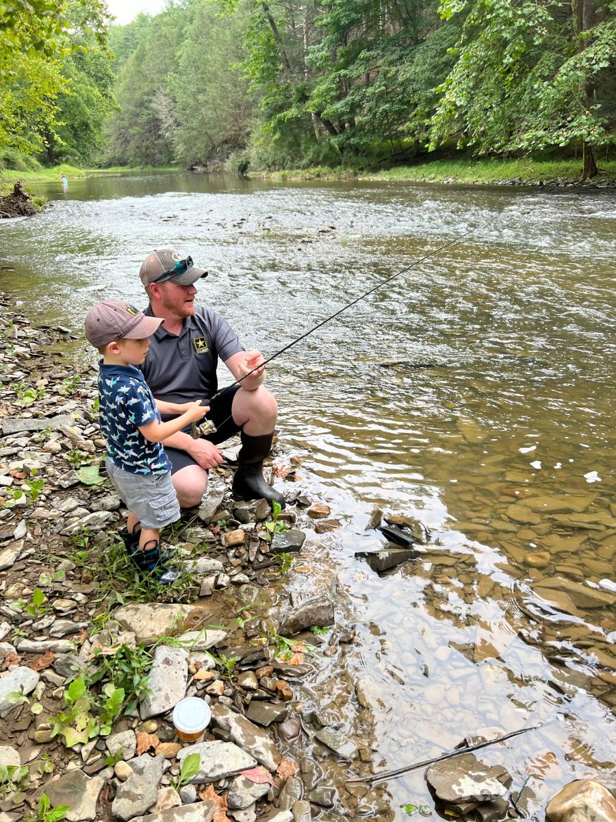 Father teaching young son to fish along the rocky shoreline of Town Creek in Flintstone, Maryland, surrounded by forested mountains