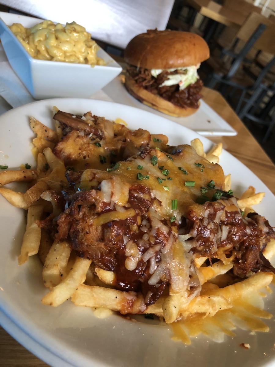 Image of plate of loaded fries with pulled pork sandwich in background.
