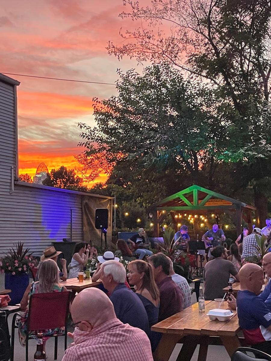 Image is of the outside patio at Coaches Corner where there are people sitting at picnic tables and a band playing in the background.