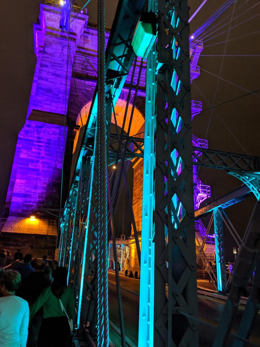 Up close on the Roebling Suspension Bridge with the cables lighted purple and teal for BLINK Cincinnati