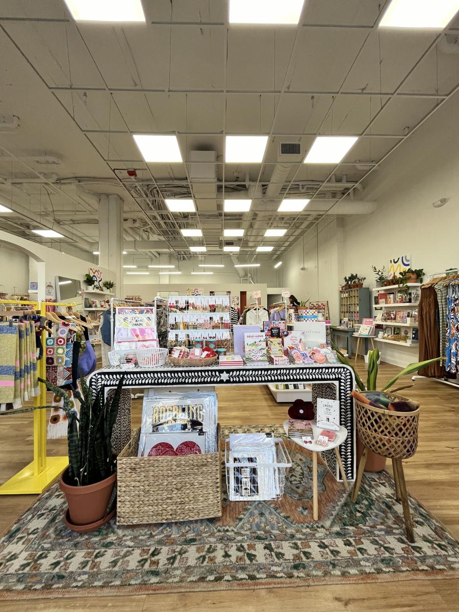 Image is of the inside of Handzy Shop and Studio with white walls, clothing racks filled with items and jewelry displays.