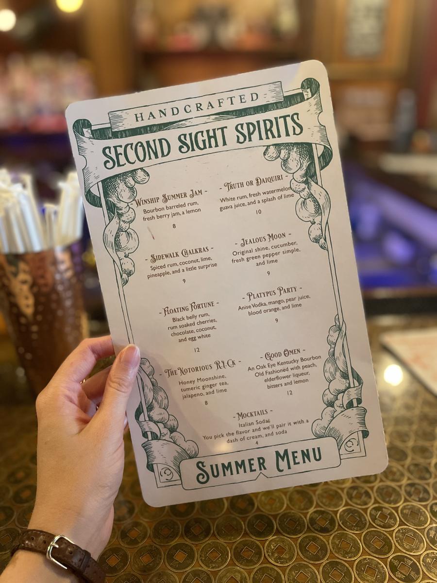 A hand holding the summer cocktail menu for Second Sight Spirits.
