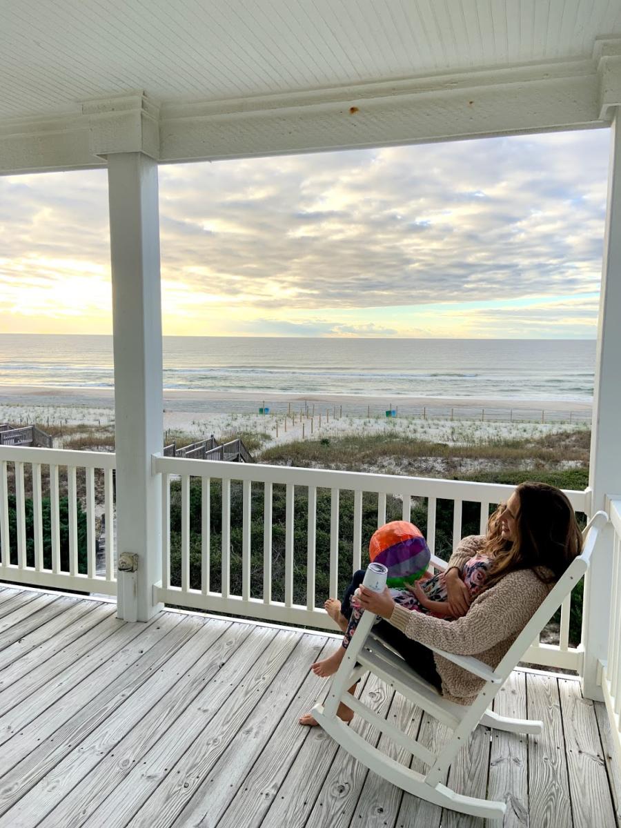 A mother and child relax in the presence of beachfront views from the porch of their rental home.