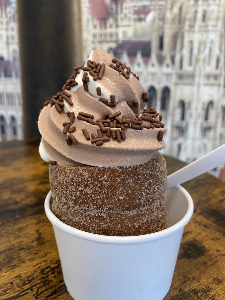 Half of a chimney cake topped with soft serve ice cream and chocolate sprinkles in a cup