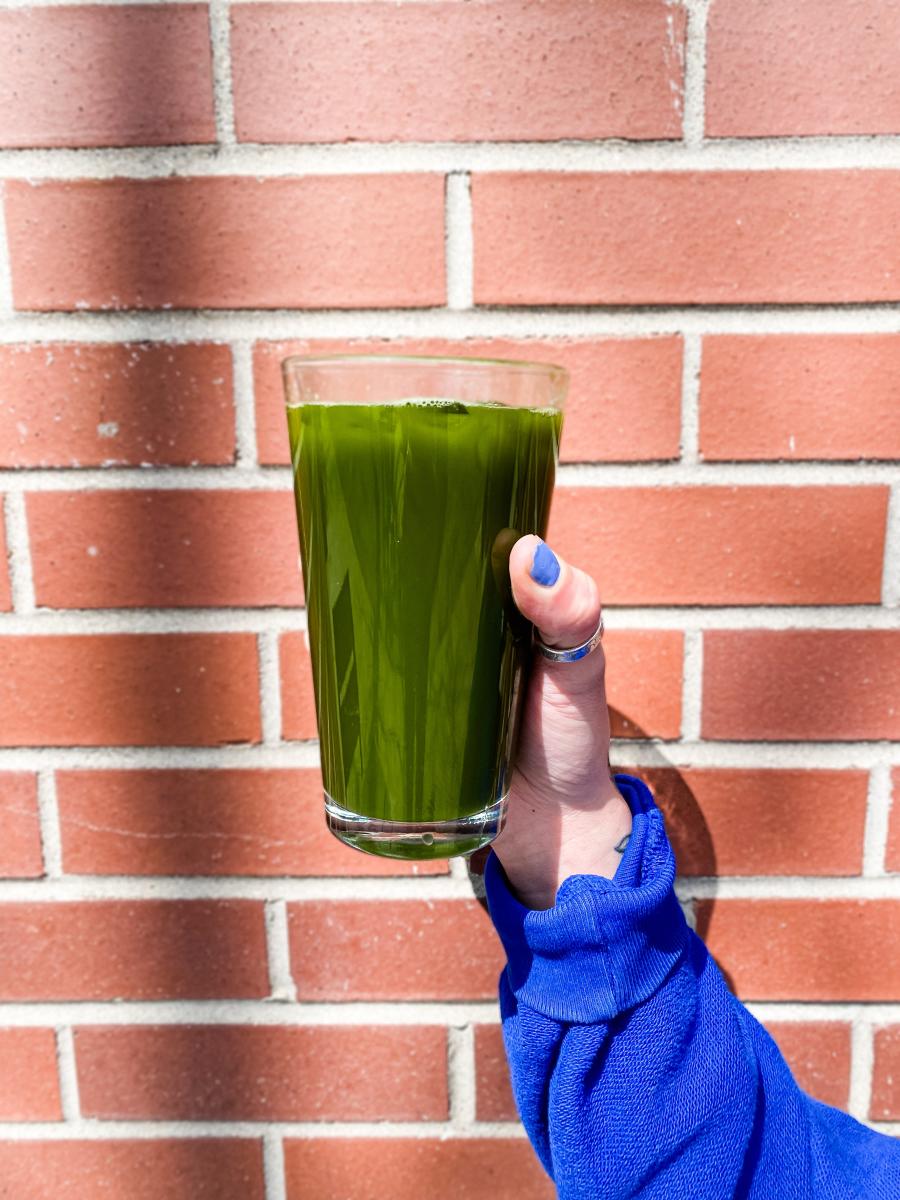 A green drink in a glass being held in front of a brick wall.