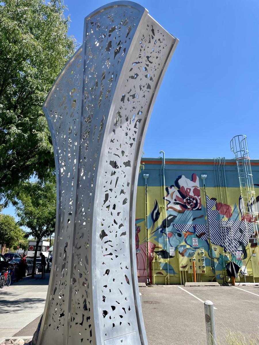 a abstract metal sculpture with a mural of flowers and leaves in the background