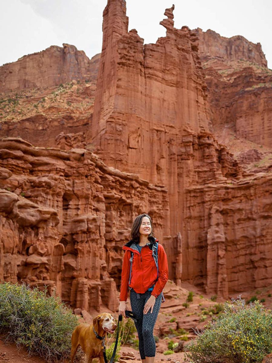 A woman in a red jacket hiking with her dog in Moab.