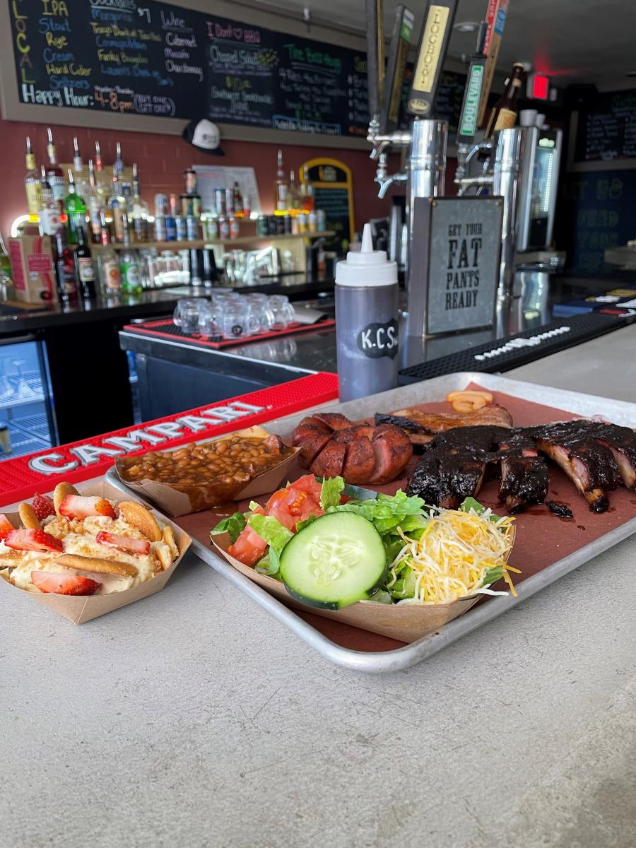 platter with salad, ribs, baked beans, and vanilla pudding; background has beer taps