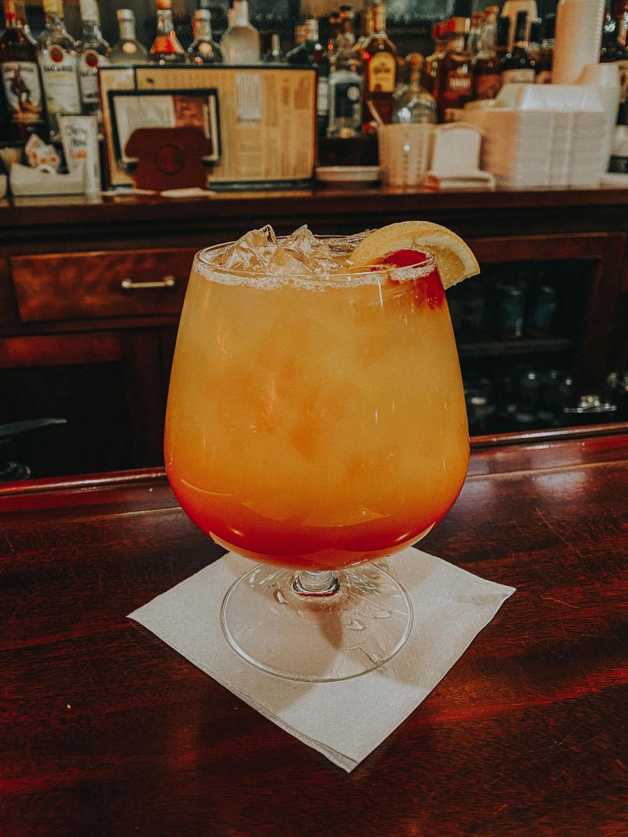 a wide cocktail glass holds a layered beverage with an orange slice on the rim