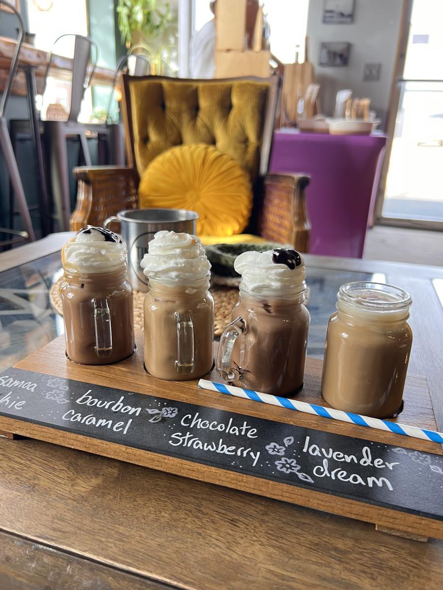 A coffee flight with four lattes in small glass cups.