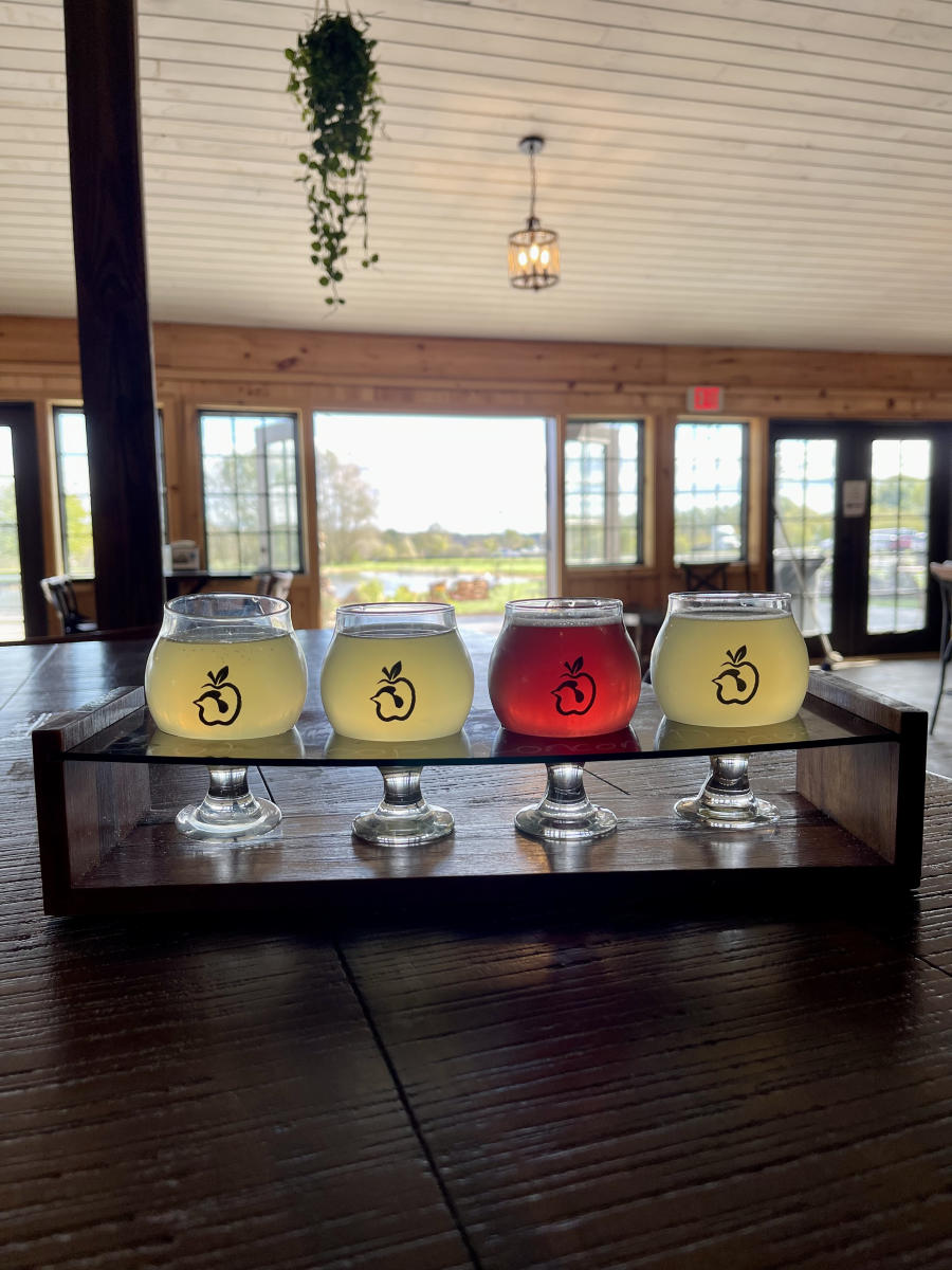 A flight of four ciders served on a wooden tray sitting in the tasting room of Henway Hard Cider