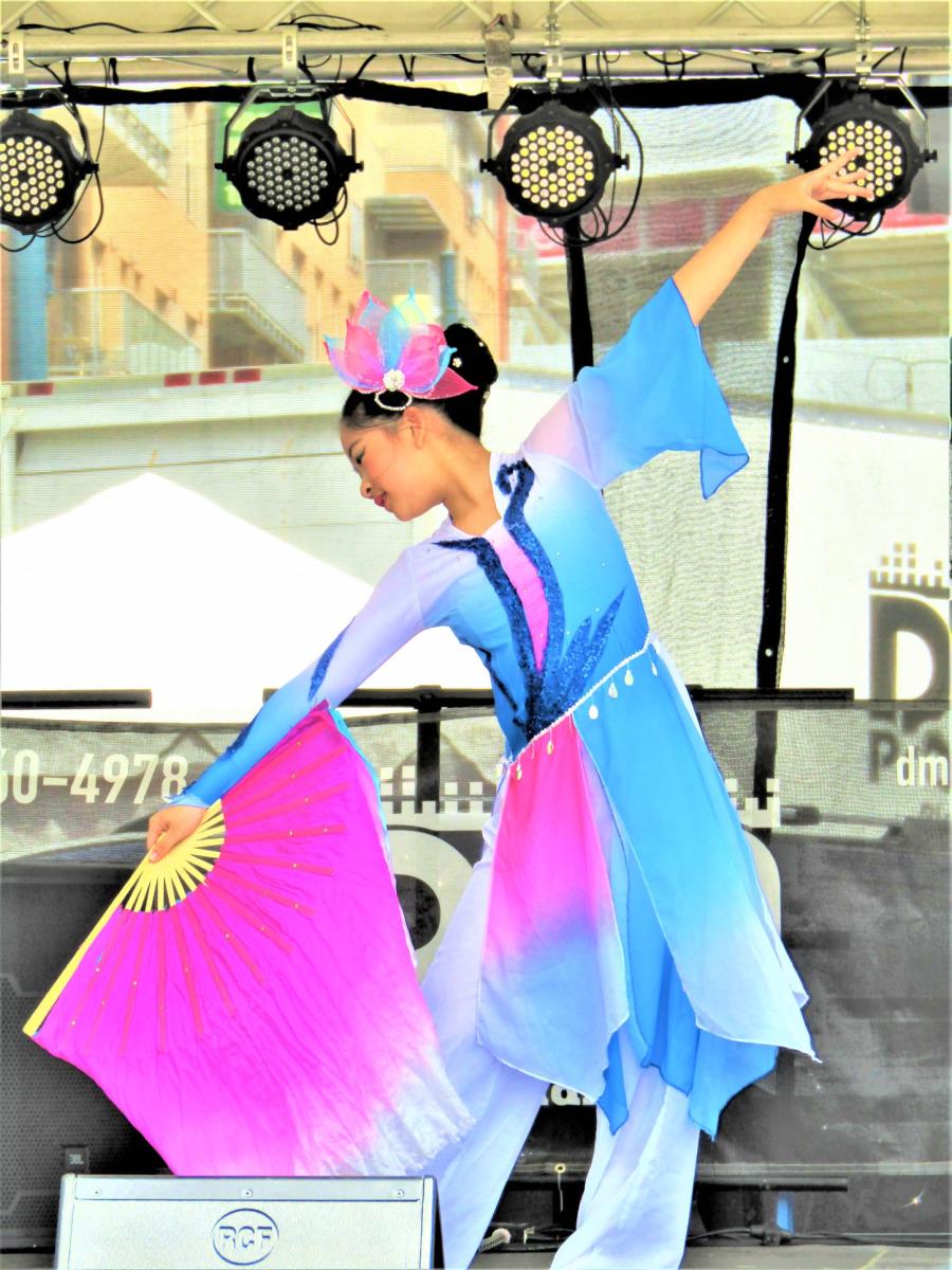 Young woman performing traditional Asian dance in a blue and pink outfit, using a large pink fan