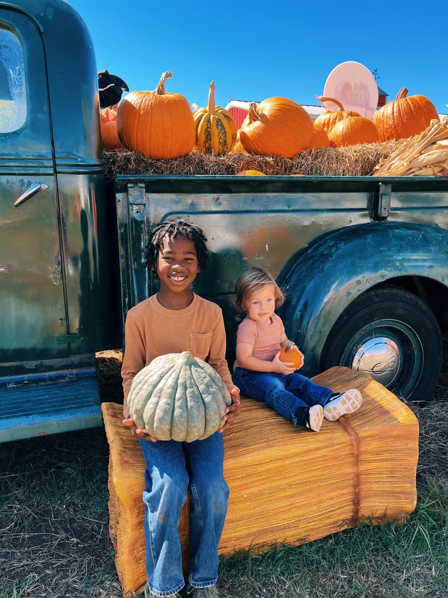Two young boys sitting on a haystack with pumpkins in front of a rustic truck at Orr Family Farm's Fall Festival