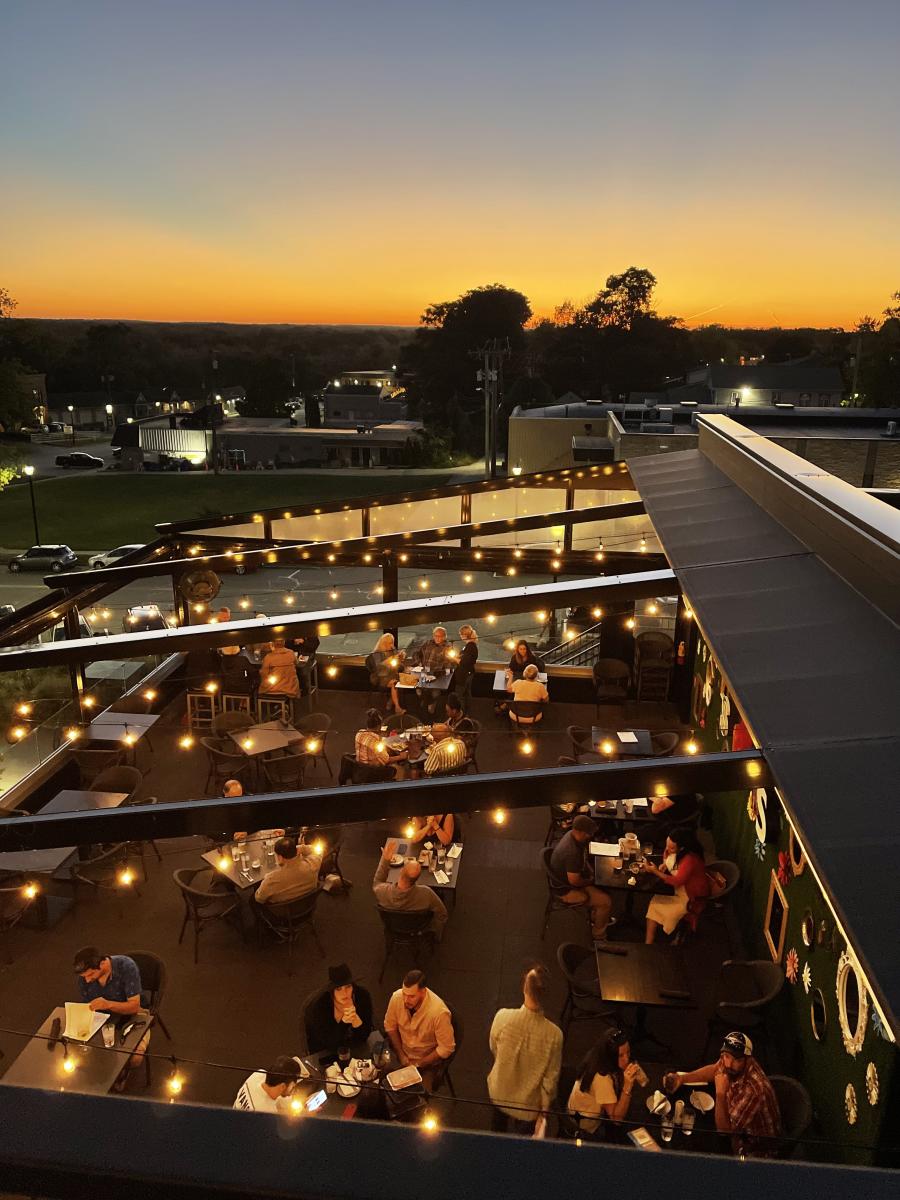 An aerial view of diners on a rooftop bar. The sun is setting in the background