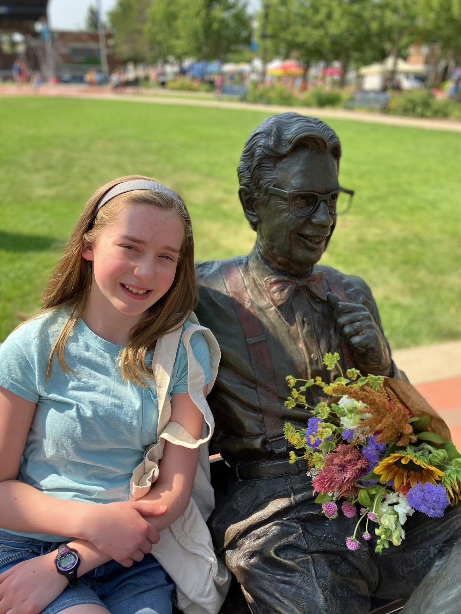 A young woman sits next to a statue of a man. A bouquet of flowers is on his lap.