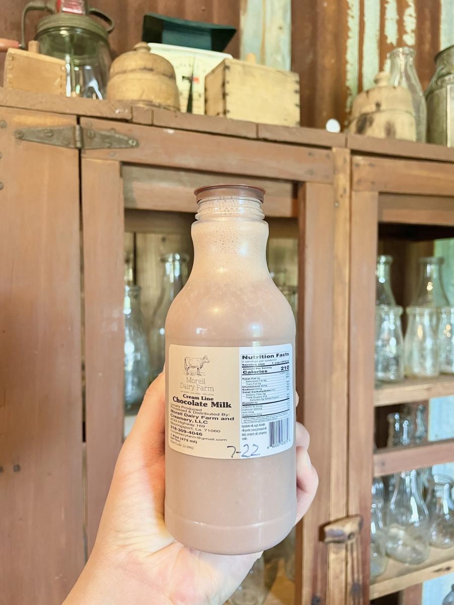 A person holding up their glass bottle of delicious chocolate milk in front of a wooden cabinet at Morell Dairy Farms.
