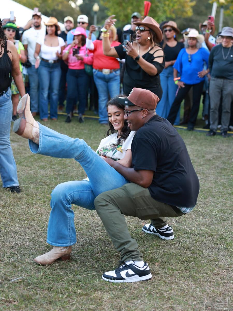 A smiling couple shows off their zydeco dance moves, with the woman kicking one leg high as a crowd of cheering festivalgoers watches at NOLA Zydeco Fest in Slidell.