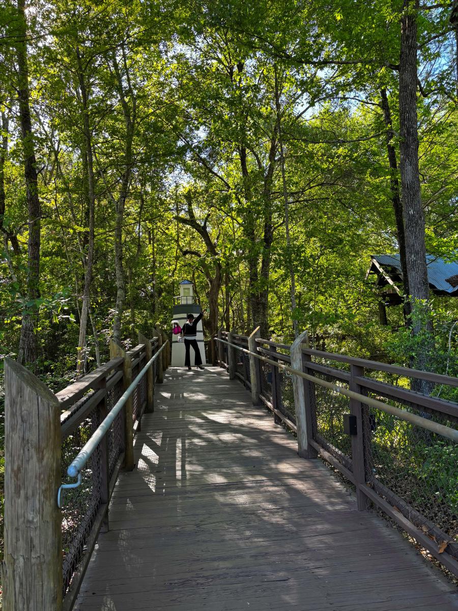 Senior Sales Manager and podcast co-host Zondra White Jones waves from the wooded boardwalk near the lighthouse at the Visit The Northshore Visitor Center in Mandeville, Louisiana.