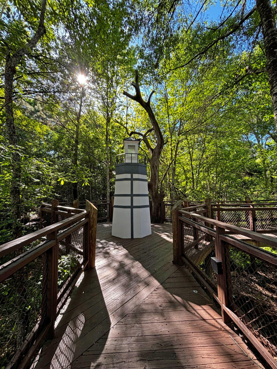Boardwalk entrance and decorative lighthouse structure surrounded by wooded wetlands at the Visit The Northshore Visitor Center in Mandeville, Louisiana.
