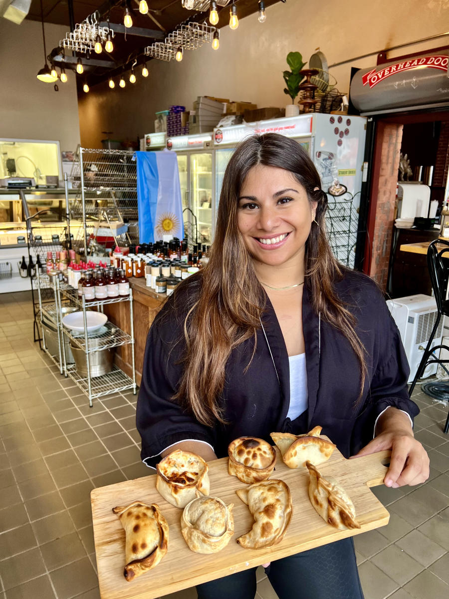 Carolina Freeman, chef and co-owner of Argentina's Empanadas, smiles as she poses with an assortment of freshly made empanadas