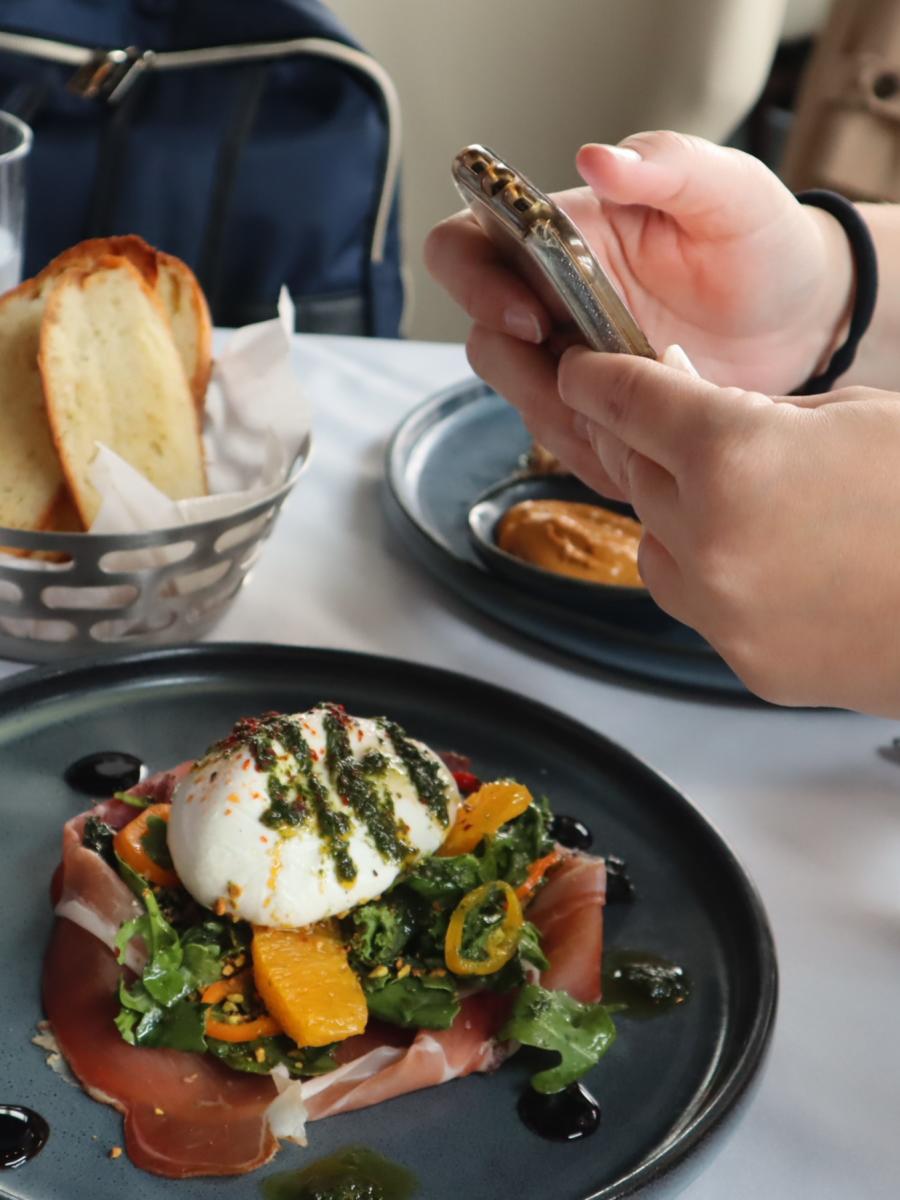 Person holding phone, taking photo of food at Azzurro Italian Coastal Cuisine in The Woodlands, Texas