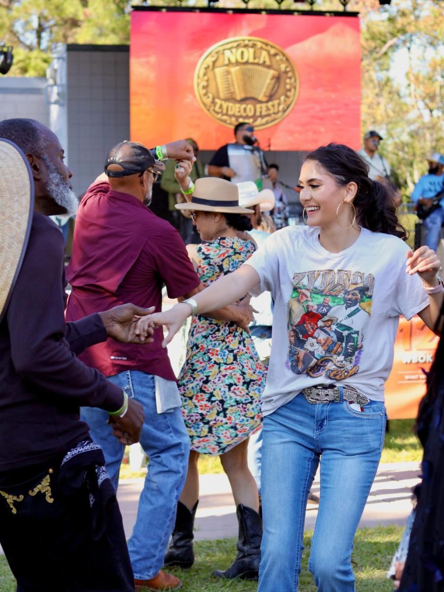 Festivalgoers dance together in front of a stage with live musicians and a large NOLA Zydeco Fest sign at Heritage Park in Slidell.