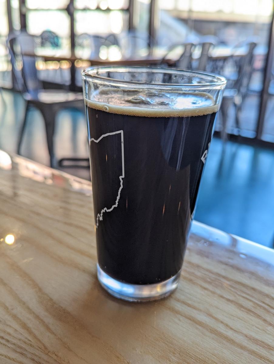 Image is of a dark, stout beer in a pint glass on the table.