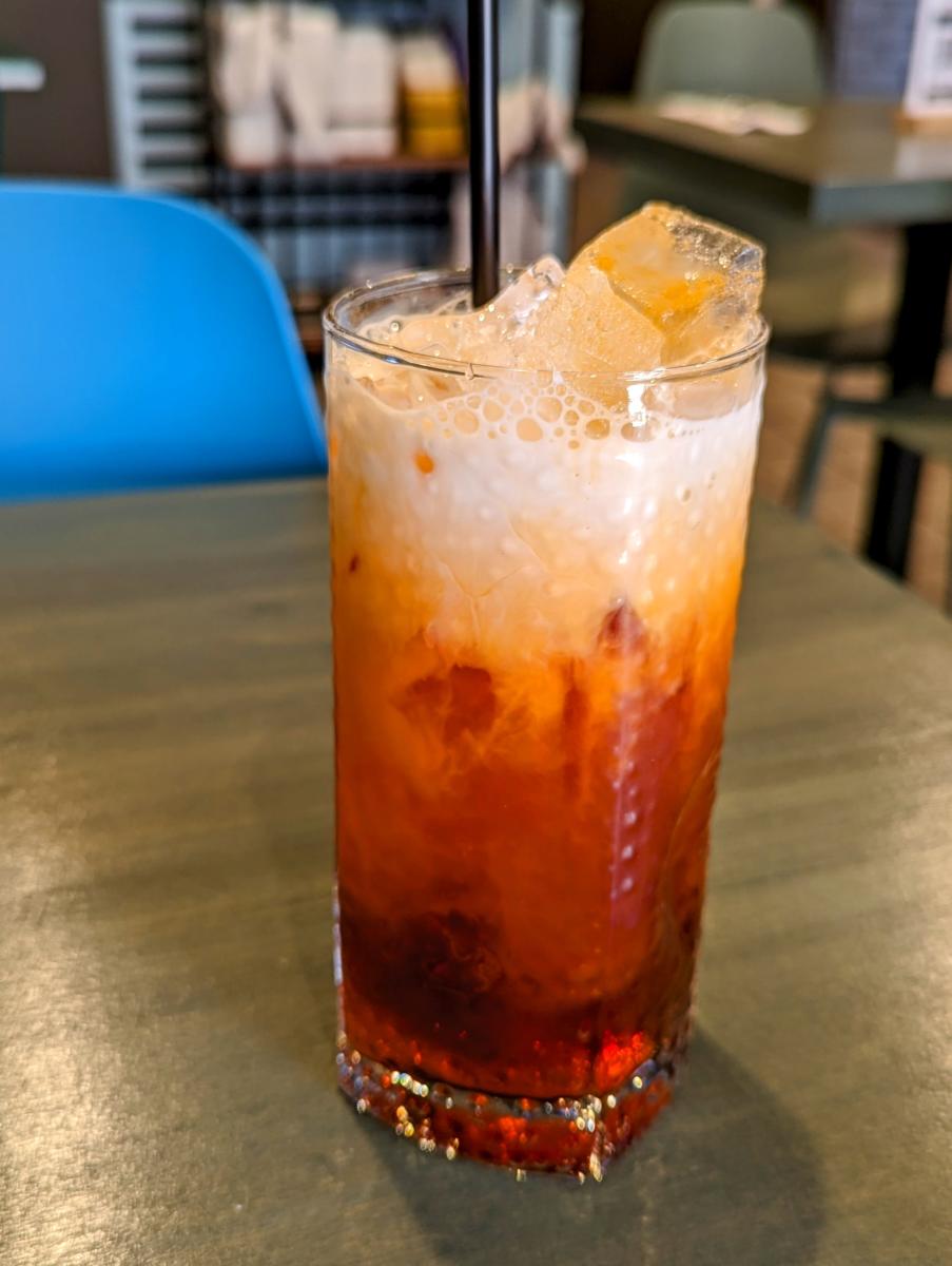 Image is of an iced tea with heavy cream at the top, ice and a straw.
