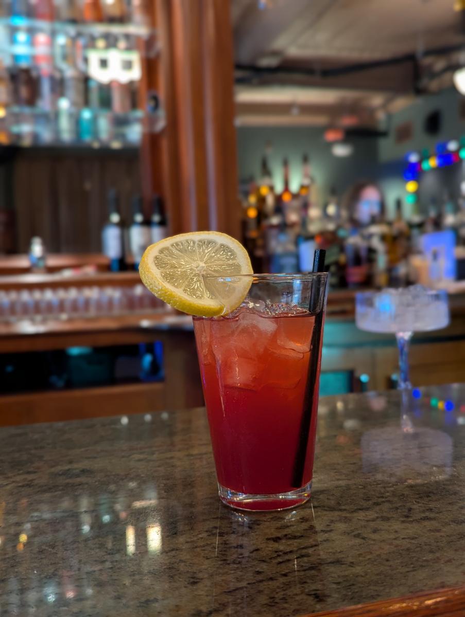 A red, iced drink with a lime sits on the counter at Alley Cat.
