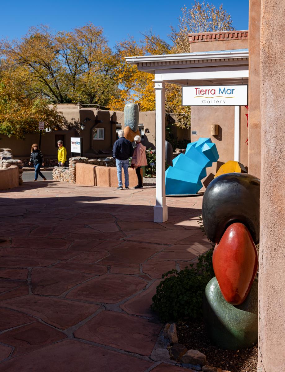 People walking past Tierra Mar Gallery in a courtyard with colorful sculptures and a vibrant, sunlit setting.
