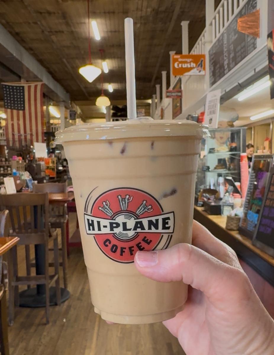 hand holding a cup of iced coffee from Hi Plane Coffee inside UG White