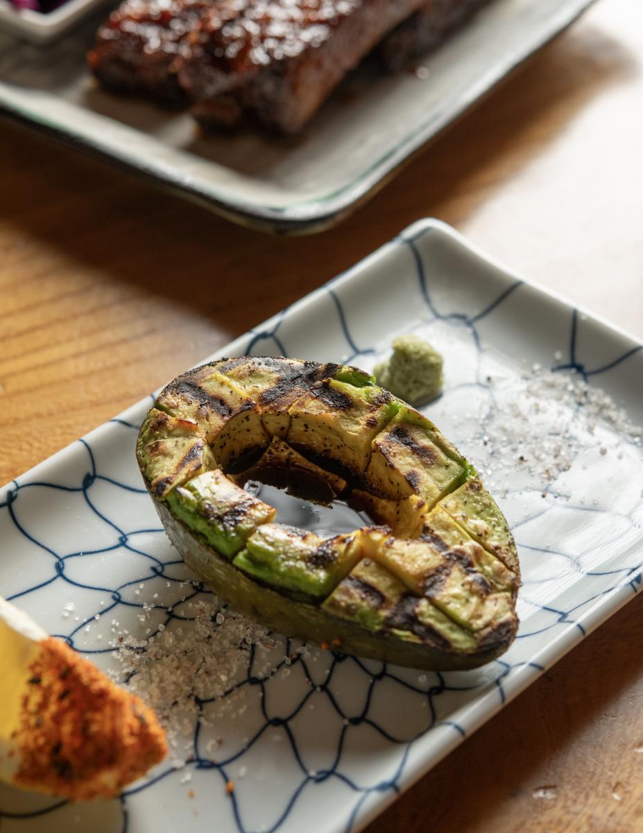 Grilled avocado on a patterned plate with salt and a seasoned lemon wedge.