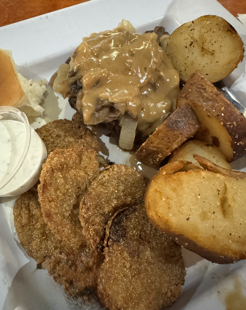Plate of food featuring hamburger steak with mushrooms, onions, and gravy, with sides of fried green tomatoes and fried taters.