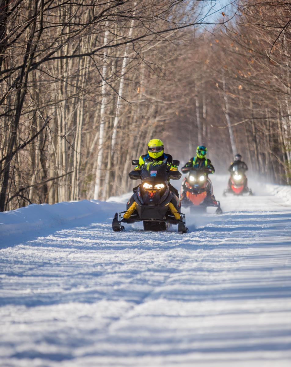 Three People Riding Snow Mobiles In Big Bay