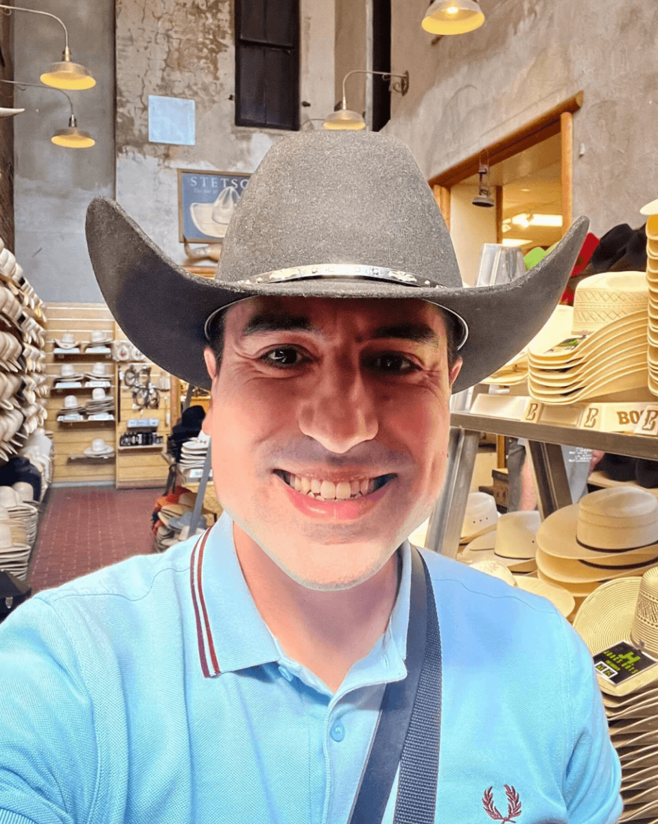 Smiling man taking a selfie trying on a cowboy hat inside The Wrangler, a famed Cheyenne store for ranch wear.