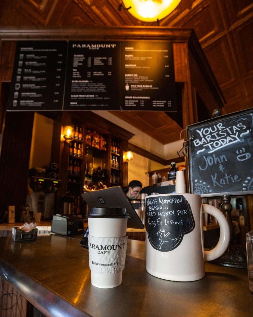 A cup of coffee with the word "PARAMOUNT CAFE" written on it, sitting on a counter.