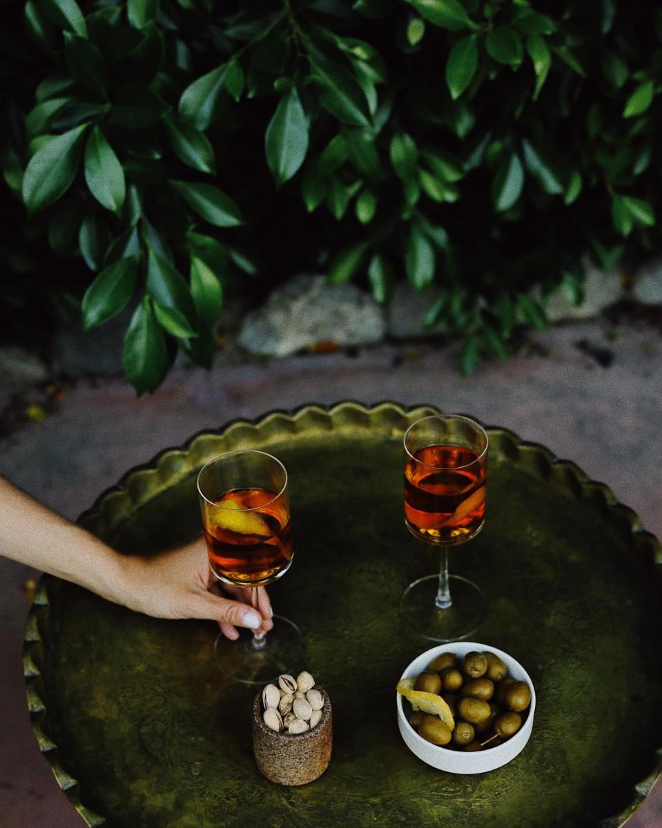 The image is of two glasses filled with drinks and next to it, two bowls. Once of olives and one of nuts.