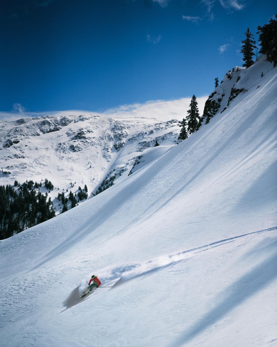 A person skiing down a snowy slope with a mountain covered in snow in the background.