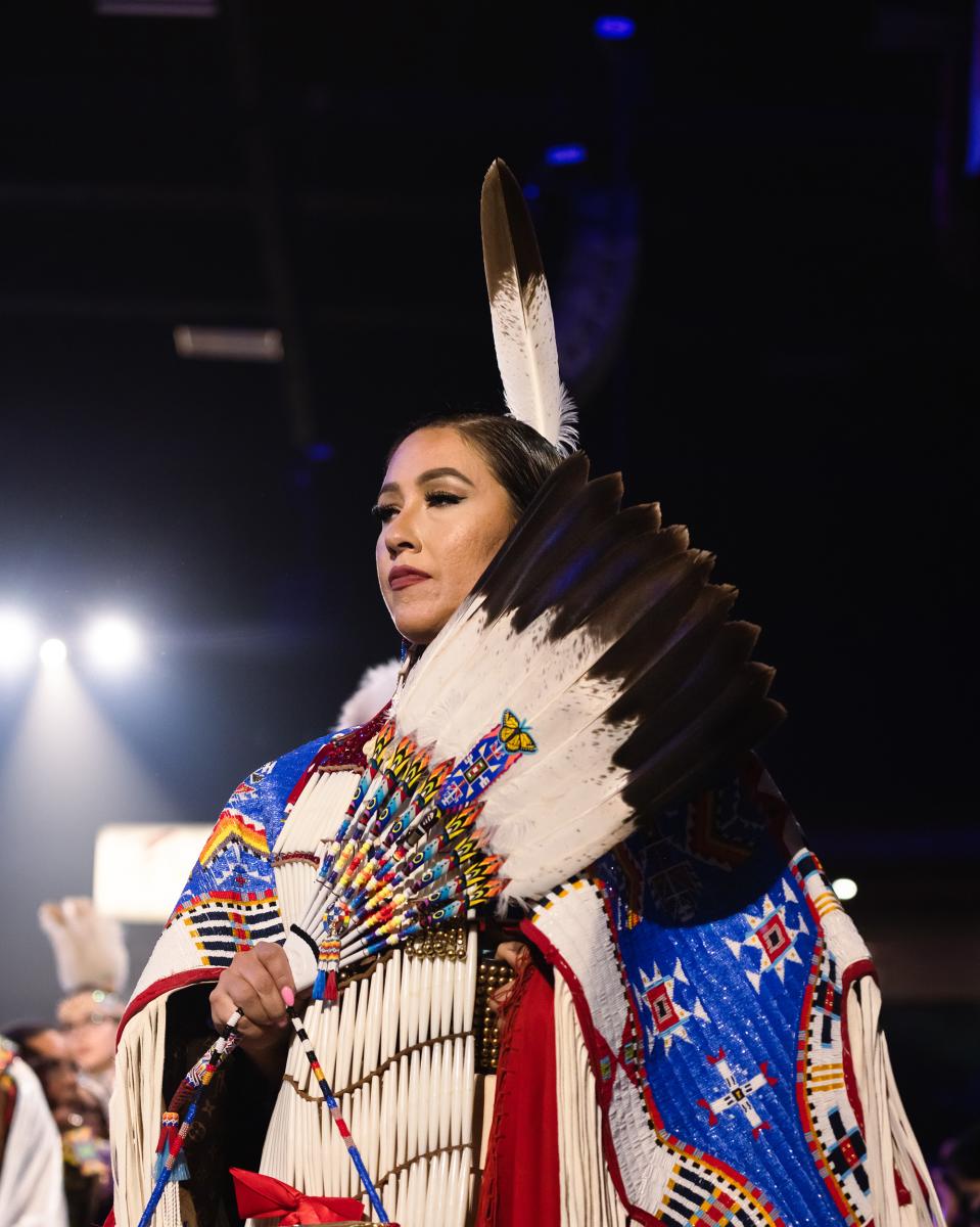 Randi Bird (Sioux) performs in the  Women’s Traditional Dance, where the feet never leave the ground, signifying a connection to the earth. The slow steps keep the long fringes swaying gently. Dancers raise an eagle-feather fan at significant moments of the song.
