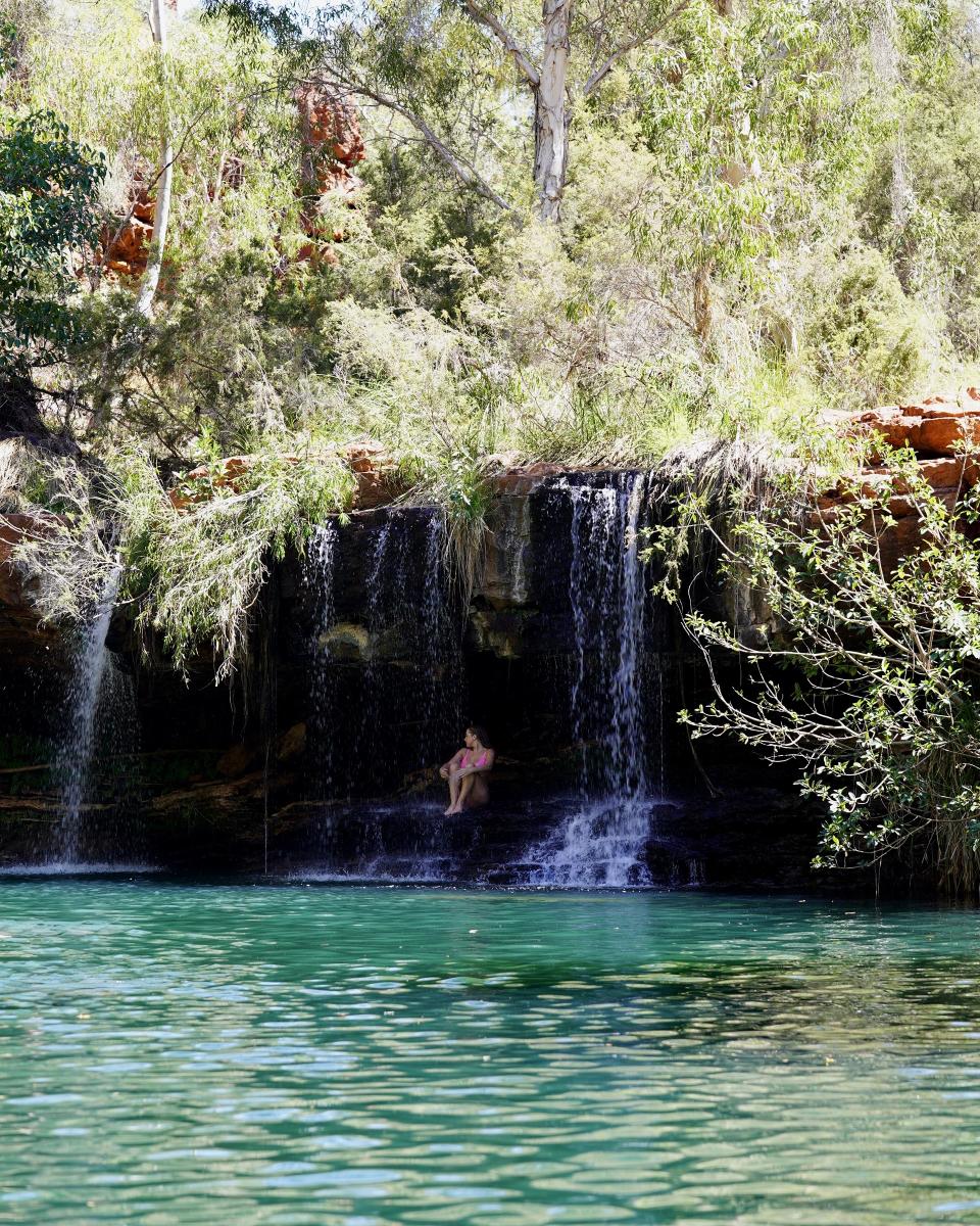 A woman sitting under the waterfall at Fern Pool in Karijini National Park