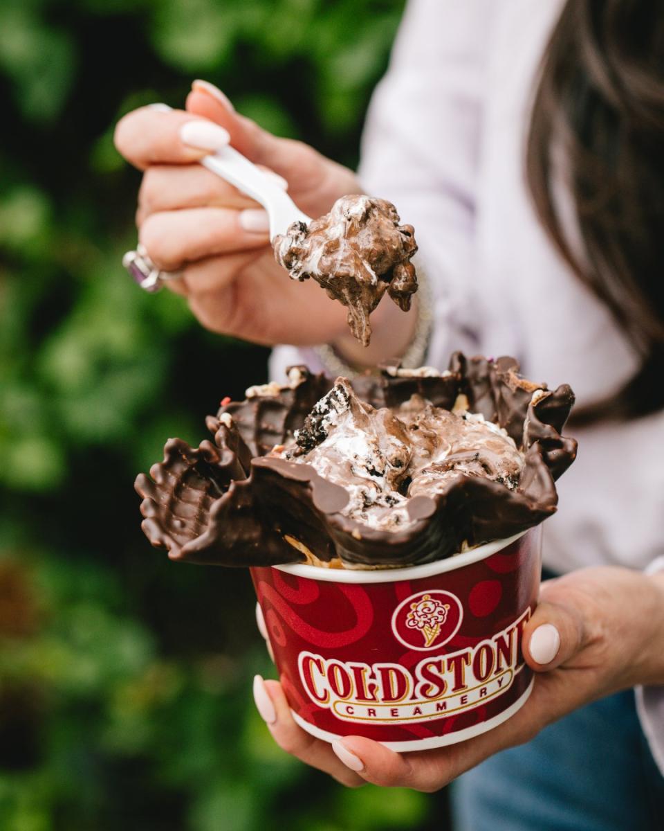 A woman holding a cup with a chocolate waffel bowl in it and chocolate ice cream with brownie pieces.