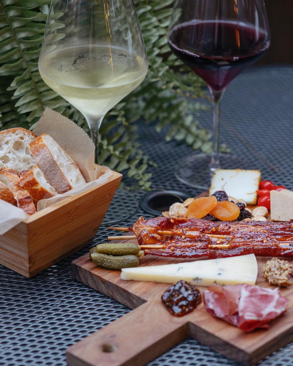 Image is of two glasses of wine, one red and one white, a breadbasket and a charcuterie board.