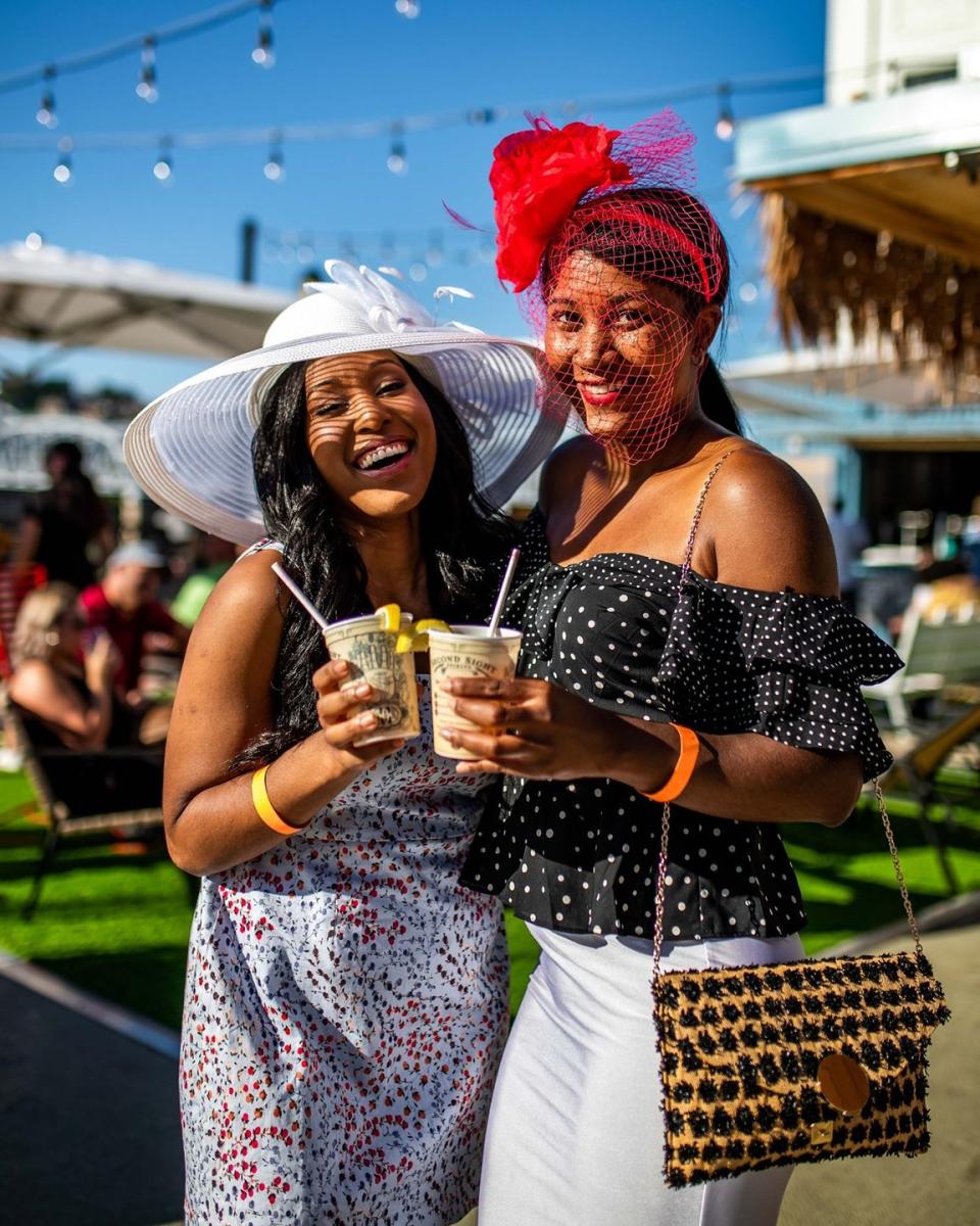 Image is of two ladies wearing derby hats and holding mint julep drinks on Derby Day.