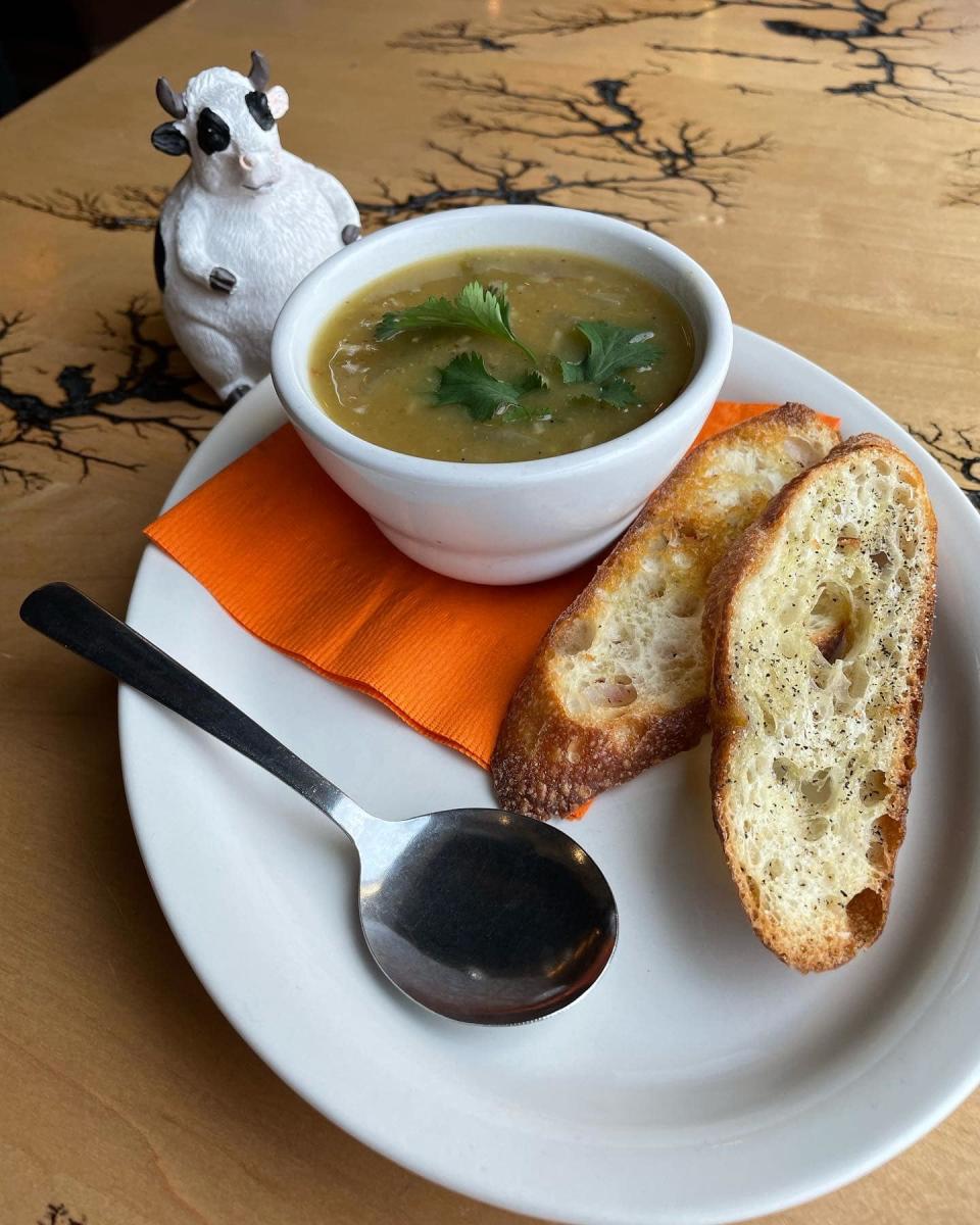 Image of a white plate on a wood table with two pieces of crostini next to a small white bowl with soup.