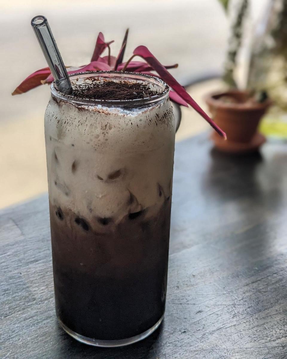 Iced coffee with a dusting of crusted Oreo cookie on top in a glass mug with a straw.