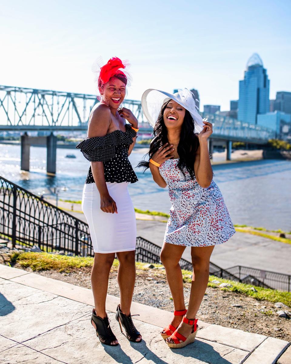 Two women laughing on the Newport Ky. riverwalk with the Cincinnati skyline and Ohio river behind them