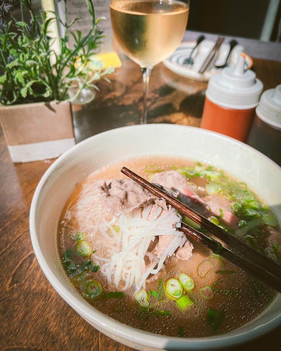 Bowl of beef pho with a glass of wine in the background.