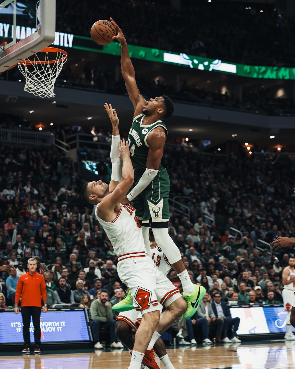 A Milwaukee Bucks player leaps toward the basket for a layup over a Chicago Bulls defender during a packed home game at Fiserv Forum.